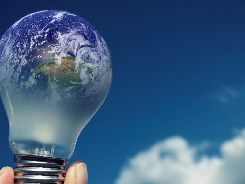 Lâmpada com espectro do planeta terra com plano de fundo um céu azul com nuvens simbolizando economia de energia elétrica e sustentabilidade